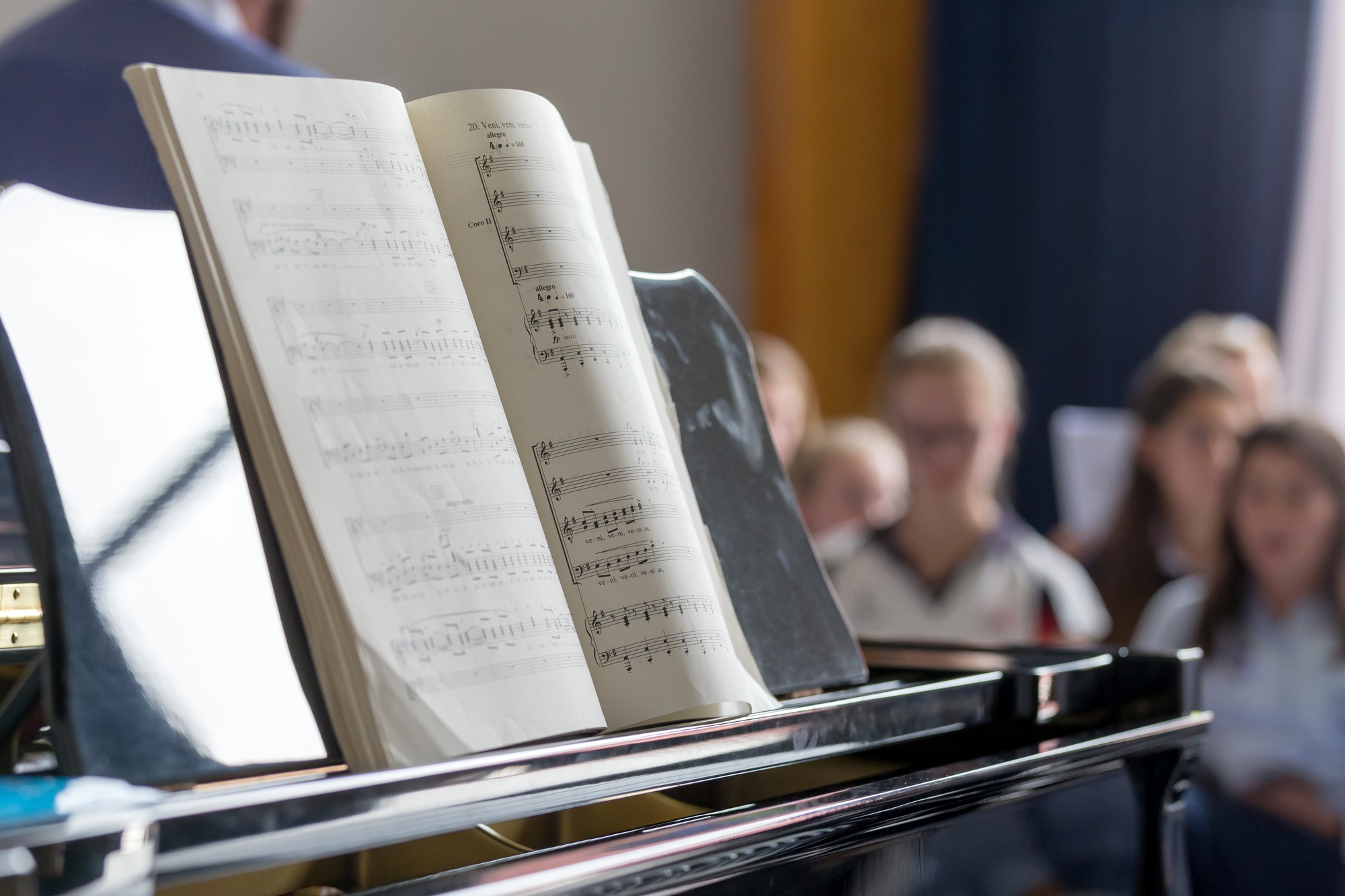 School choir, piano with notes on foreground and students defocused at the background School choir, piano with notes on foreground and students defocused at the background
